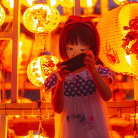 お祭りの提灯に囲まれスマホに夢中の浴衣姿の女の子の写真