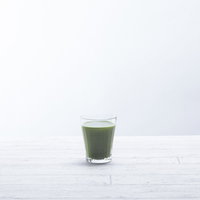 白いテーブルに置かれた青汁一杯の栄養ドリンクの写真