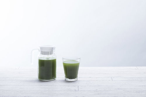 濃い緑色の青汁が入ったポットとグラス、白い背景