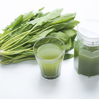 新鮮なほうれん草の束とガラスポットに入った青汁の写真