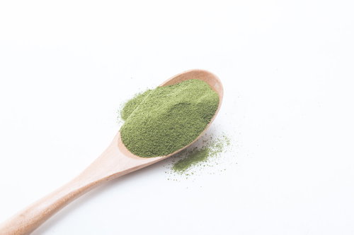 白い背景に落ちる粉末青汁とスプーン、栄養補助食品