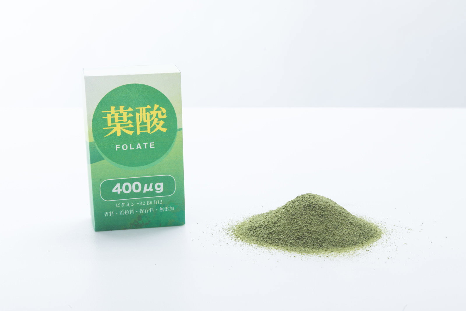 白い背景に置かれた緑色の葉酸パッケージと抹茶色の青汁粉末