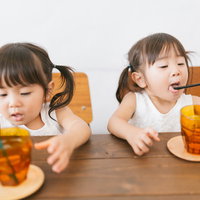 ストローでジュースを飲む何でも口にいれる小さい双子の子どもの写真