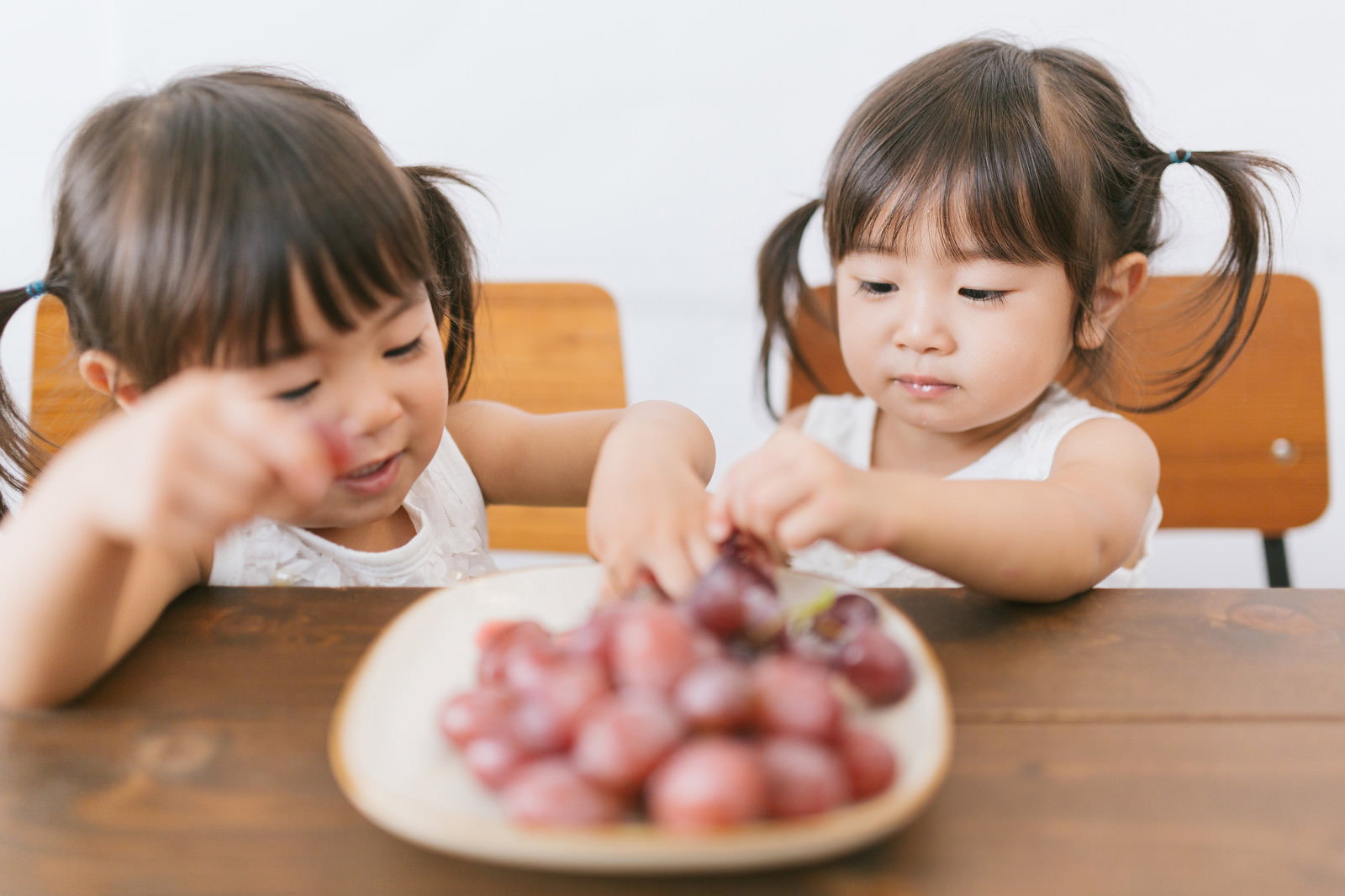 テーブルでぶどうを食べているツインテールの双子の女の子［モデル：あおみどり］