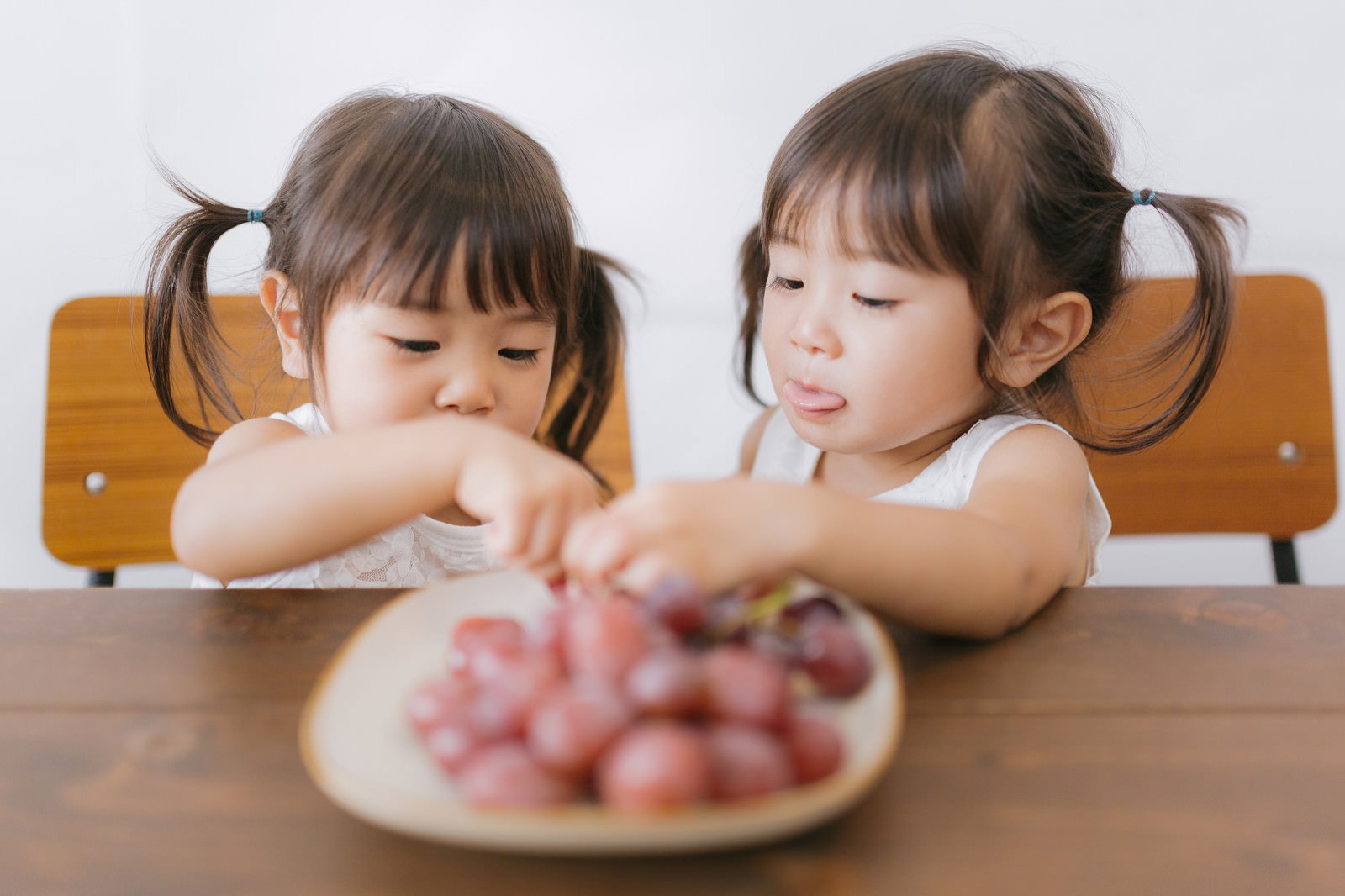 テーブルの巨峰を前に向かい合って座る双子の女の子［モデル：あおみどり］