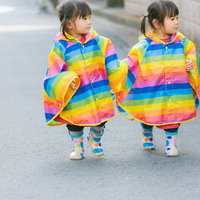 手をつないで仲良く歩くカラフルなレインコート姿の双子の写真