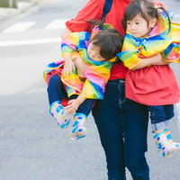 ママに抱きかかえられるカラフルな服の双子の姉妹の写真