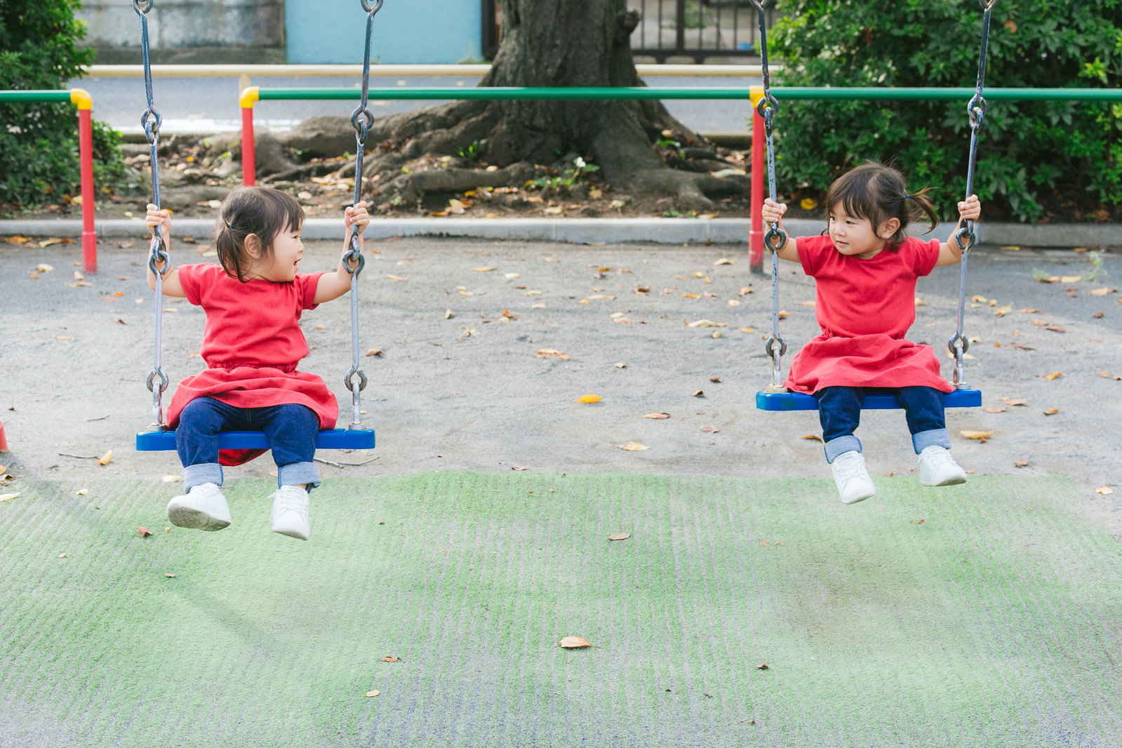 公園でブランコに並んで座り、楽しそうに遊ぶ双子の女の子［モデル：あおみどり］
