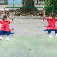 赤いシャツの双子が並んで遊ぶブランコ - 公園での兄弟姉妹の楽しい時間の写真