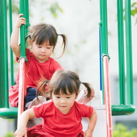 公園のすべり台で遊ぶ双子の女の子、ツインテールで楽しく滑るの写真