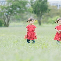 赤いワンピースのツインテール双子女児が芝生で仲良く遊ぶの写真