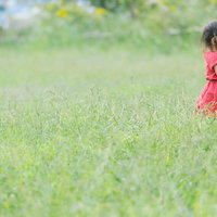 緑の原っぱで赤いワンピースを着て遊ぶ女児の写真