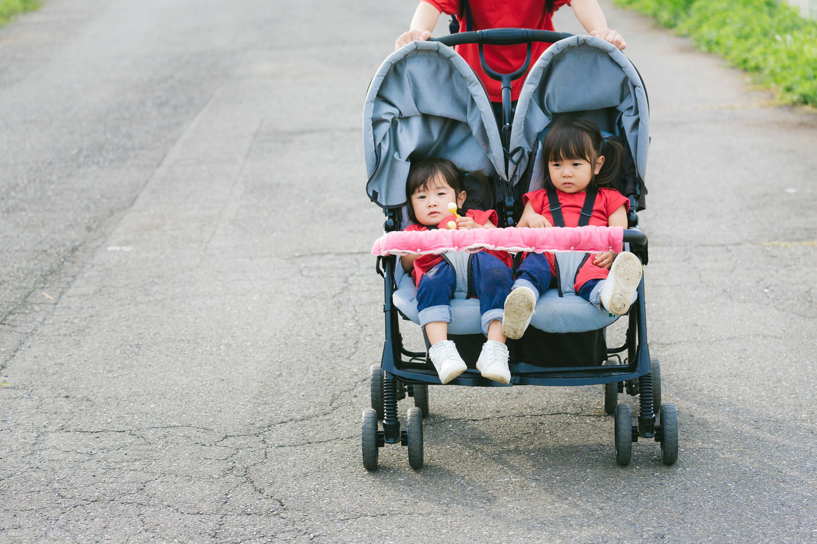 二人乗りベビーカーに乗って赤いヘルメットをかぶった双子の姉妹［モデル：あおみどり］