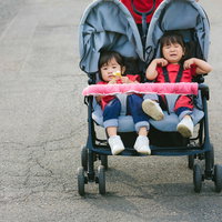 赤いベビーカーで愚図る双子の女の子の育児風景の写真