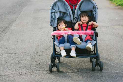 赤いベビーカーで愚図る双子の女の子の育児風景