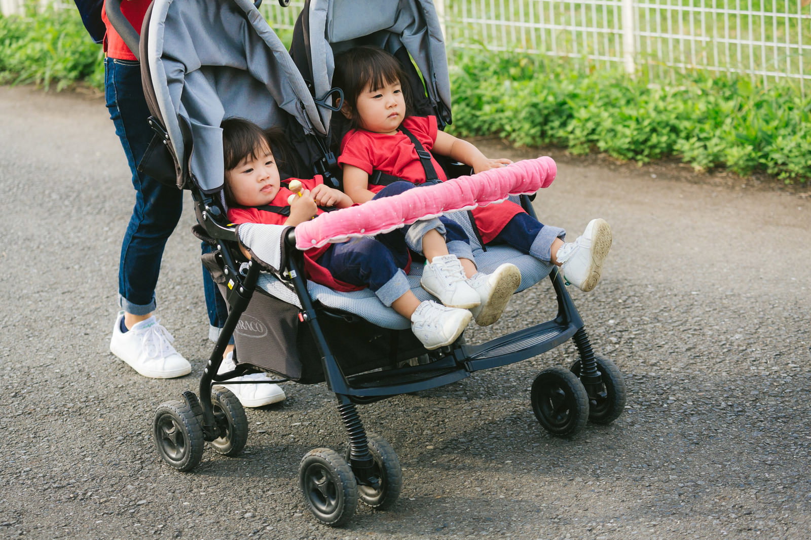 双子用の赤いベビーカーに座る二人の女の子とママの足元［モデル：あおみどり］