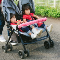 二人乗りベビーカーで屋外散歩中の姉妹と母親の写真