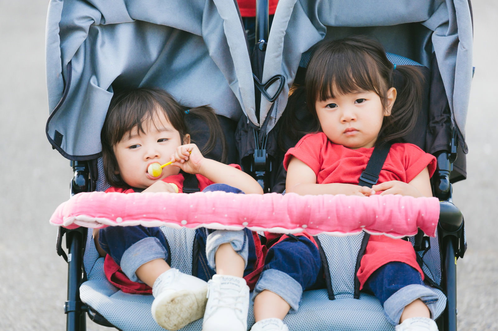 ベビーカーに座り不機嫌な表情をする双子の女の子［モデル：あおみどり］