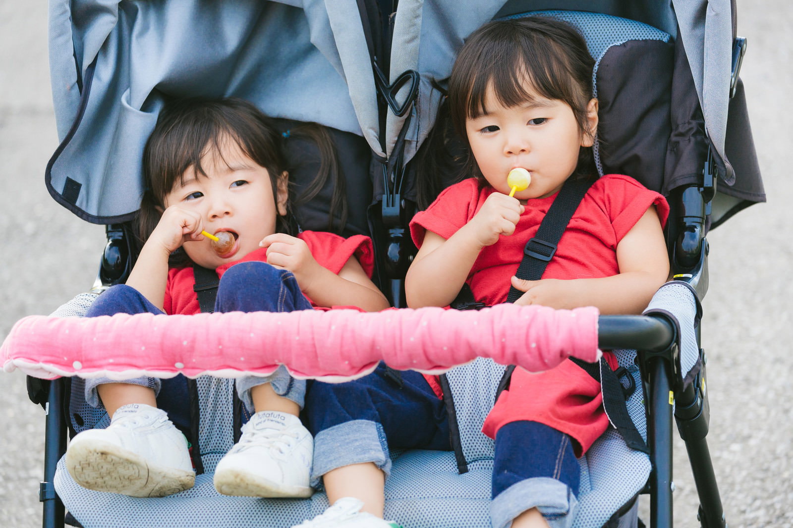 ベビーカーに座って飴を食べている双子の女の子［モデル：あおみどり］