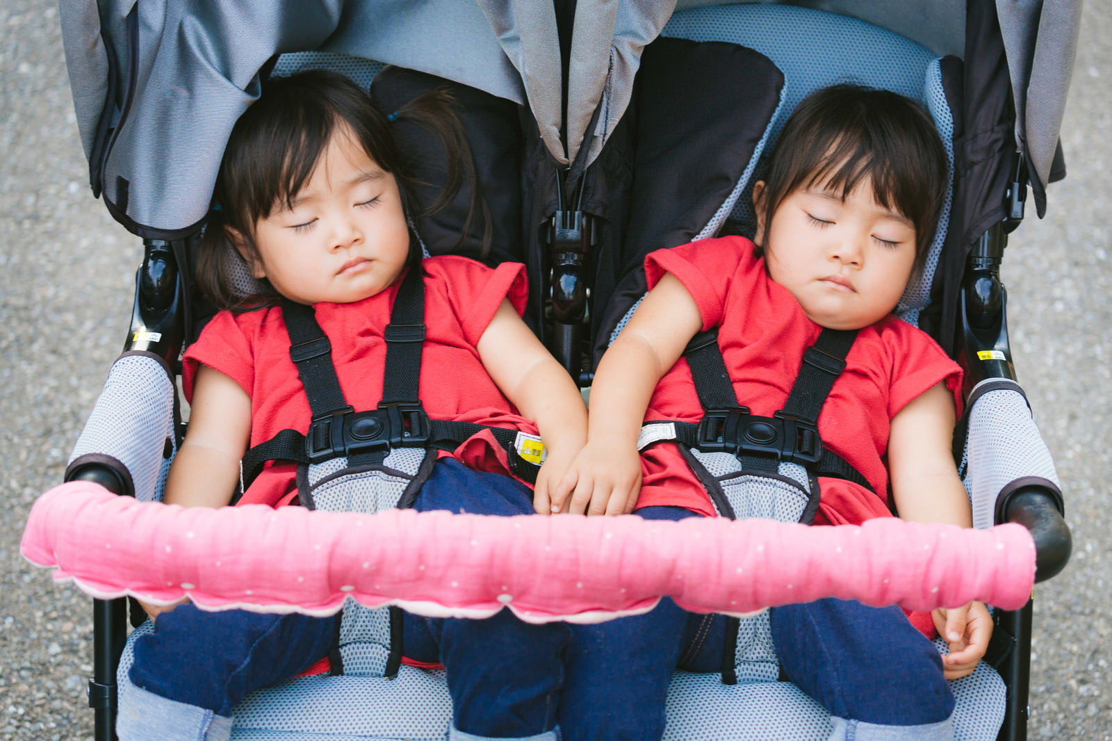 二人乗りベビーカーで赤いベストを着た双子の女の子が並んで眠っている様子［モデル：あおみどり］