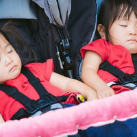 赤いウェアを着た双子の女の子がベビーカーで昼寝の写真