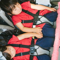 赤いライフジャケット姿でベビーカーの上でぐっすり眠る双子の女児の写真