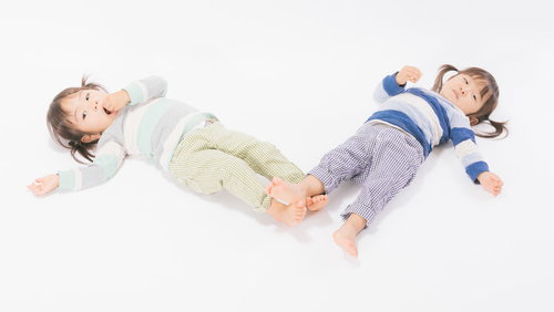 寝転ぶ姿も一緒の双子姉妹、白い背景でリラックス