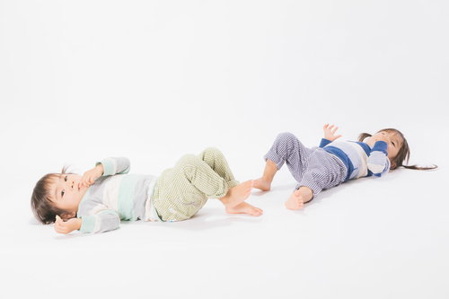 白い背景で寝そべる双子の女児、異なる色の服でリラックス