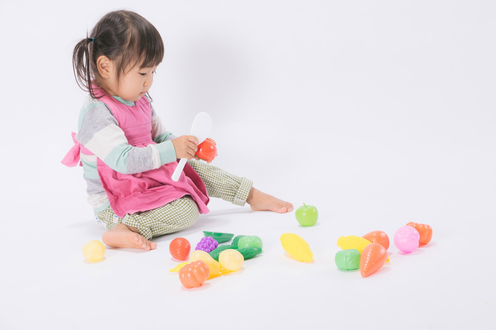 ピンクのエプロンを着てツインテールの女児がおままごとで遊んでいる様子［モデル：あおみどり］