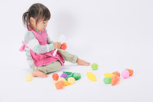 ピンクのエプロンを着ておままごとに夢中の女児