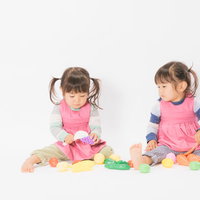 ピンクのエプロン姿でおままごとをする双子姉妹の写真