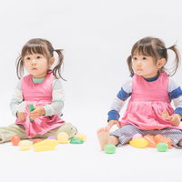 ピンクのエプロンを着ておままごとする双子の子供の写真