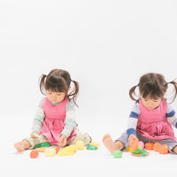 ピンクと紫のエプロン姿でおままごとをする双子女児の写真