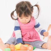 ピンクのエプロンを着けてツインテールにした女の子のままごと遊びの写真