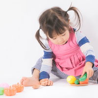 ピンクのエプロンを着けておままごと遊びをする女の子の写真
