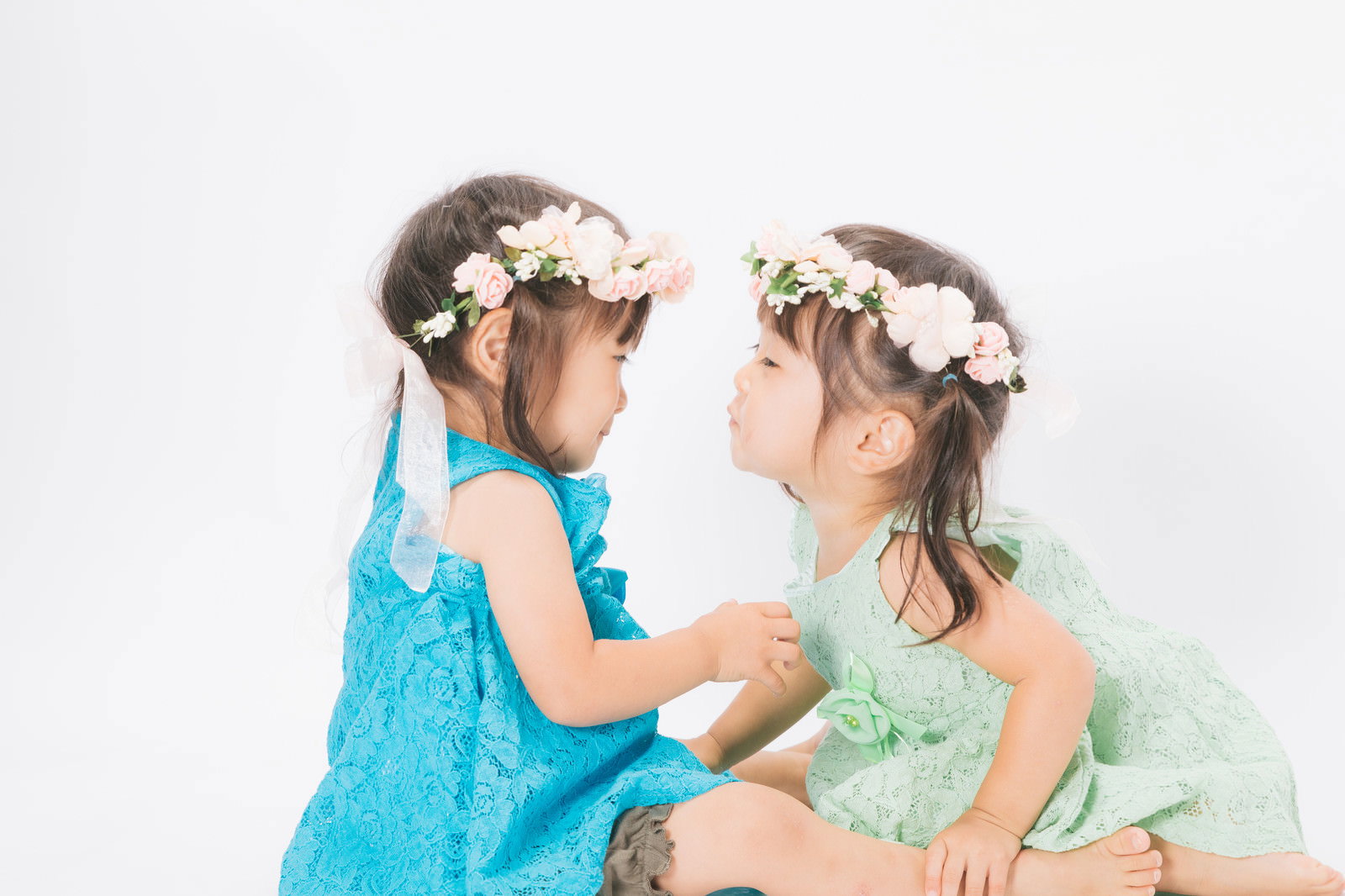花冠を付けて青と緑のドレスを着た双子の女の子がチューしている