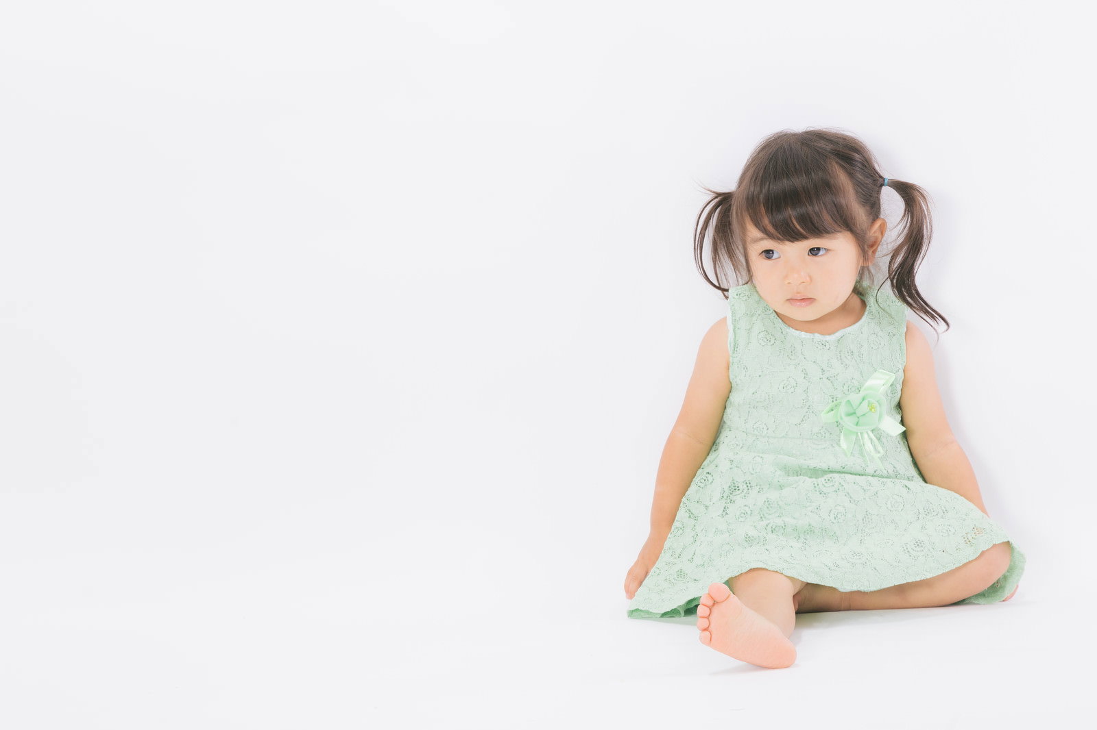 芝生に座って草を触る幼い女の子［モデル：あおみどり］