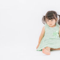 人見知りで不安な表情の女の子が芝生で草を触るの写真