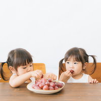 子供たちのおやつに葡萄を与えてみた、双子の女の子がテーブルで食べる様子の写真