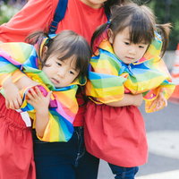 駄々をこねてぐずる双子を抱きかかえる母親の写真