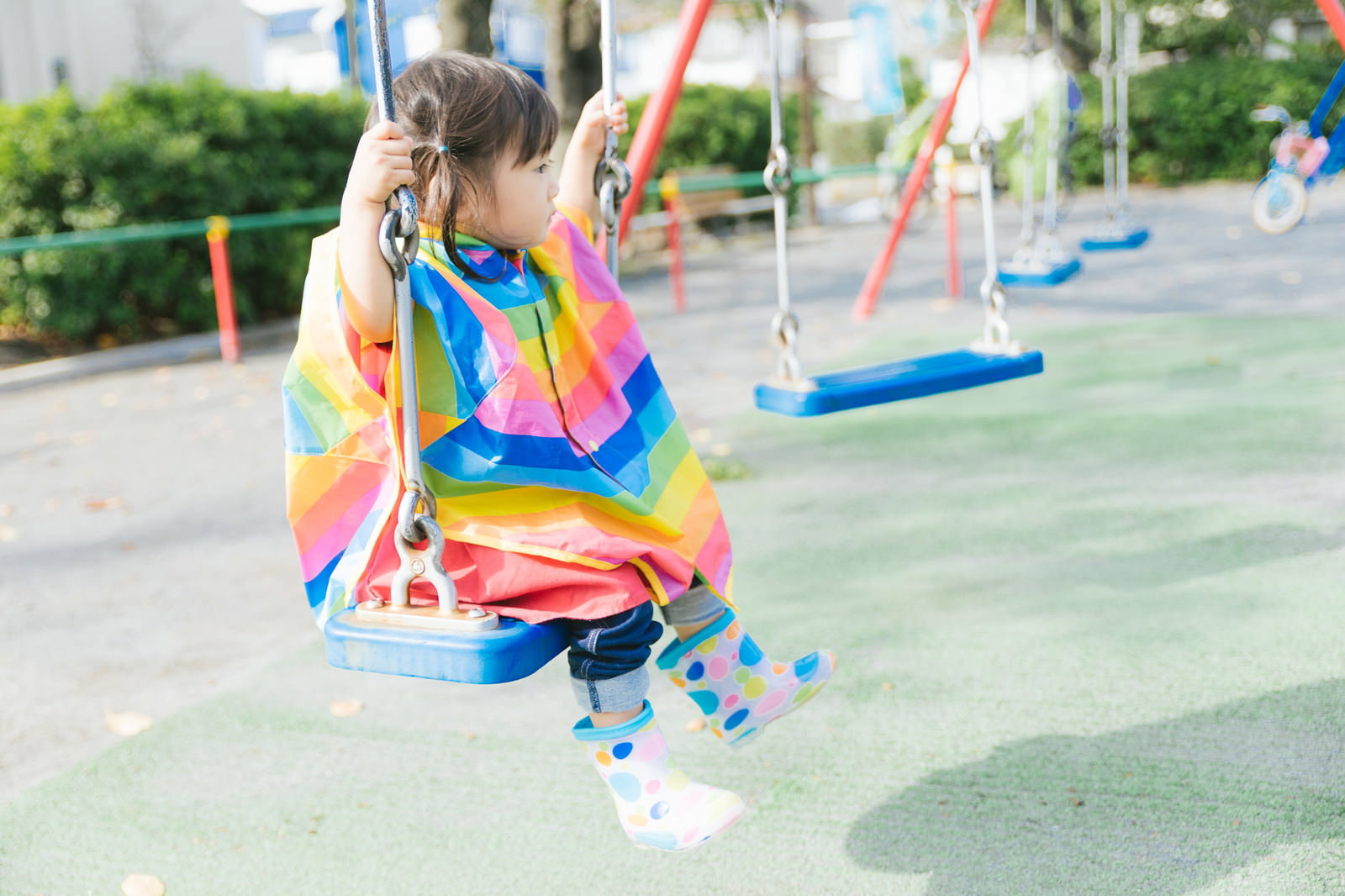 公園でブランコに座って遊ぶカラフルな服を着た女の子［モデル：あおみどり］