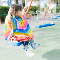 公園のブランコでちょこんと座って遊ぶ女の子の写真