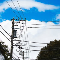 よく晴れた青空に電線が張り巡らされた電柱の写真