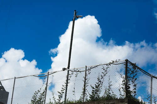 公園の柵越しに見上げる真夏空と入道雲、青く澄んだ夏の空