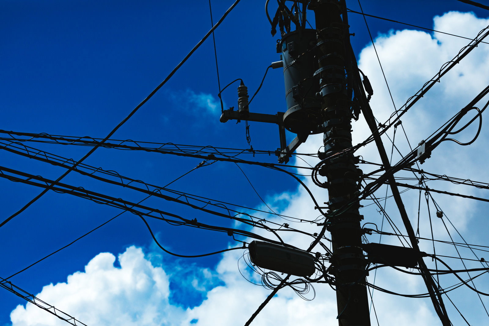 青空に浮かぶ白い積乱雲と電線が張り巡らされた電信柱のシルエット