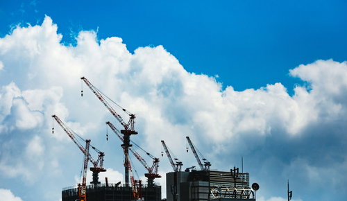 真夏の建設現場に立ち並ぶ複数のクレーンと青空