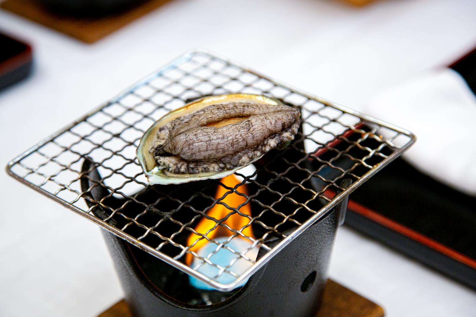 固形燃料で焼かれているあわび。網焼きされた貝が炎の上に置かれている。