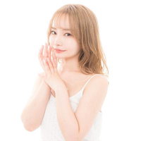 白いキャミソールで頬に手を添える透き通る肌のモデルの写真