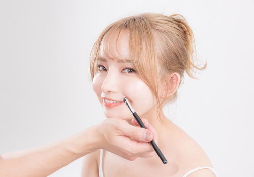 リップブラシでメイク中の美容モデル、ベージュ系メイクの透明感