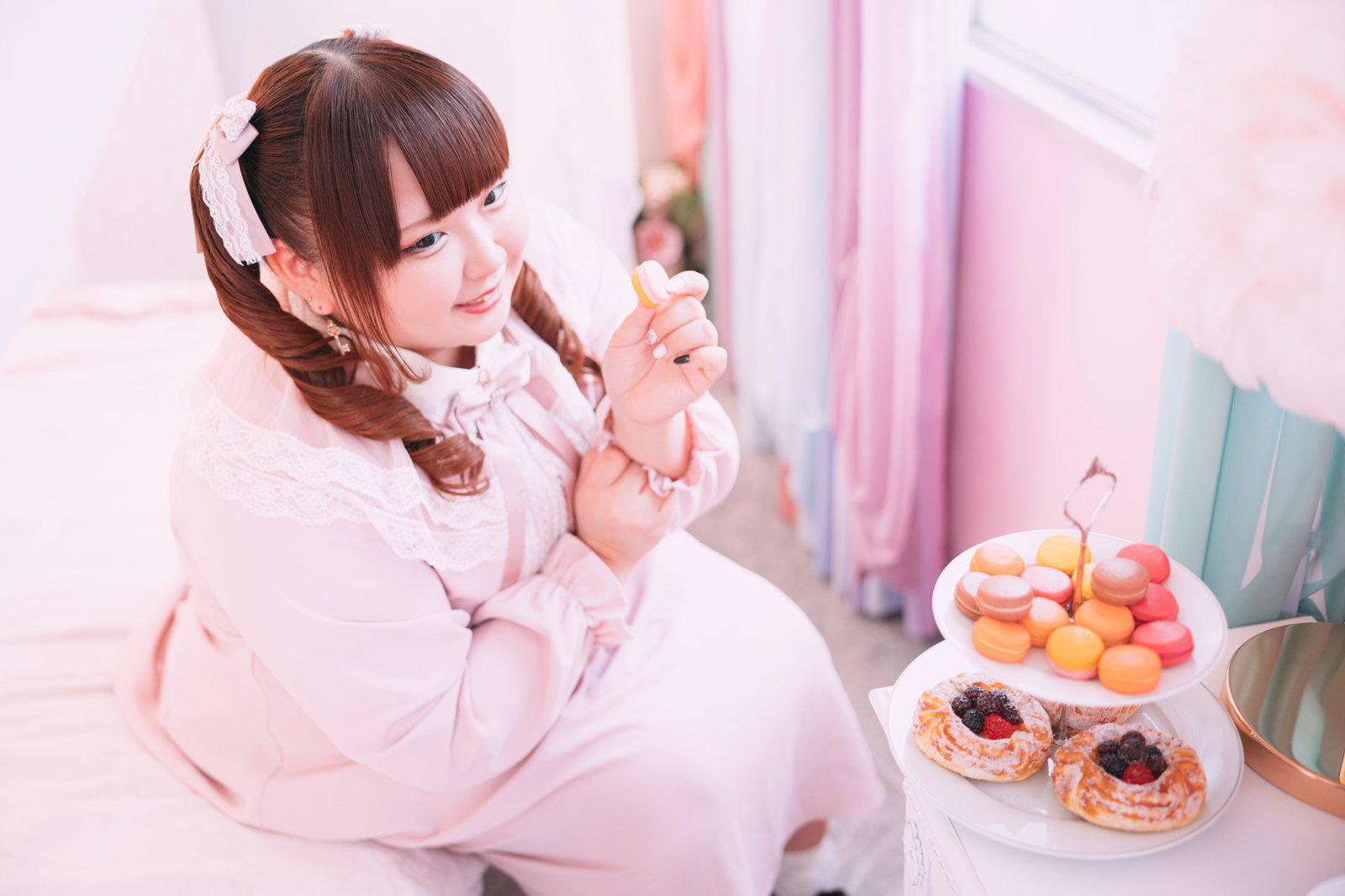 ピンクのドレスを着たツインテールの女性がマカロンを持っている［モデル：あづき］
